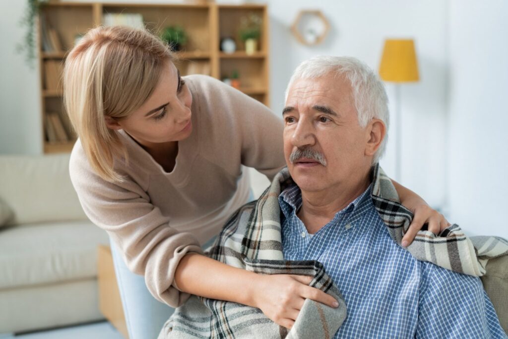A woman is helping an older man with his hair.