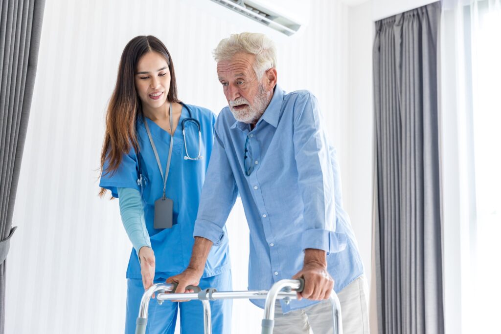 A nurse helping an old man walk with a walker.