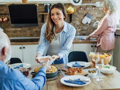 Young happy woman serving food to her father at dining table. A woman is serving food to someone at the table.