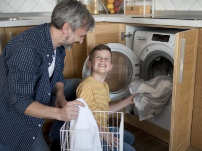 medium-shot-man-kid-doing-laundry A man and boy in the kitchen with a washer.