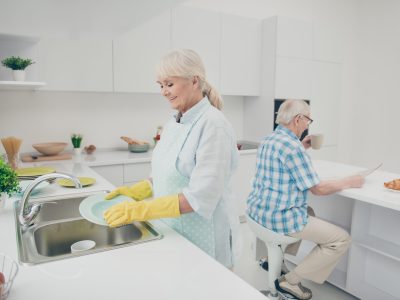 Portrait of nice cute old lady hold hand polishing drying plates A woman in yellow gloves is washing dishes.