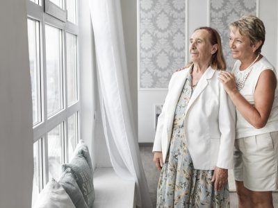 senior-mother-daughter-looking-through-window-home – Copy (2) Two women standing in front of a window.